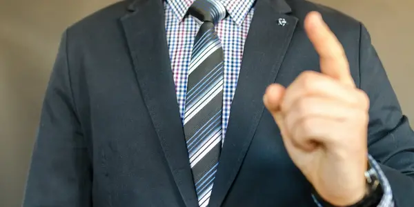 Mann im Anzug hebt den Zeigefinger f&uuml;r eine Frage