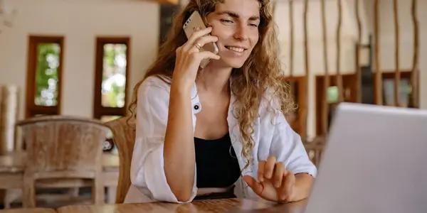 Junge Frau telefoniert l&auml;chelnd am Laptop