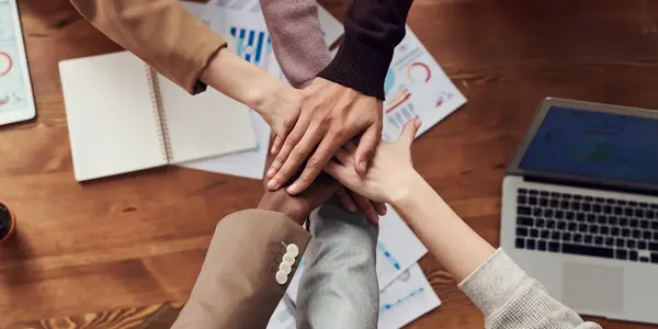 Mehrere H&auml;nde liegen im Team &uuml;bereinander auf einem Tisch