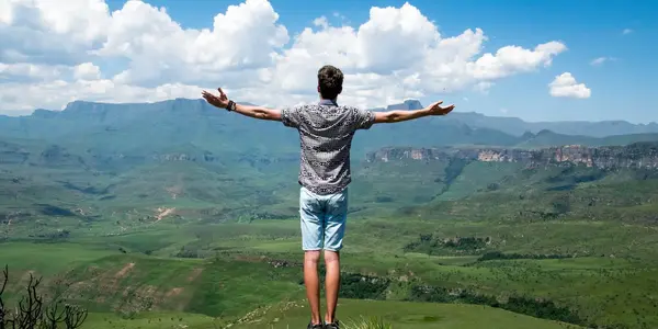 Mann steht mit ausgebreiteten Armen vor einer Berglandschaft