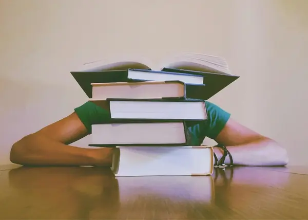 Azubi versteckt sich hinter einem Stapel B&uuml;cher